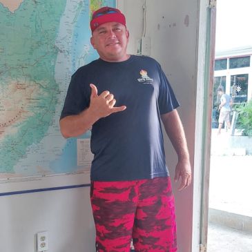 A man in red pants and a hat standing next to a map.