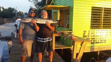 Two men holding a large fish on the dock.