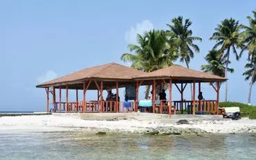 A beach with people sitting on the sand and a pavilion.