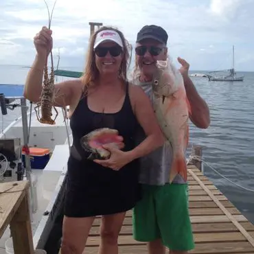 A man and woman holding fish on the dock.