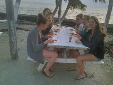 A group of people sitting at a picnic table eating pizza.