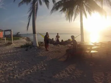 A group of people sitting on the beach at sunset.